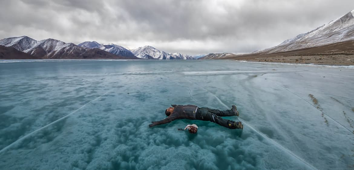 man laying on frozen pangong tso lake - frozen lakes in india